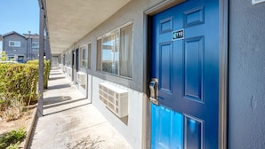A building with a blue door marked with the number 110, a covered walkway, and a row of windows. - ERTH INN by AGA - Mojave (Mojave)