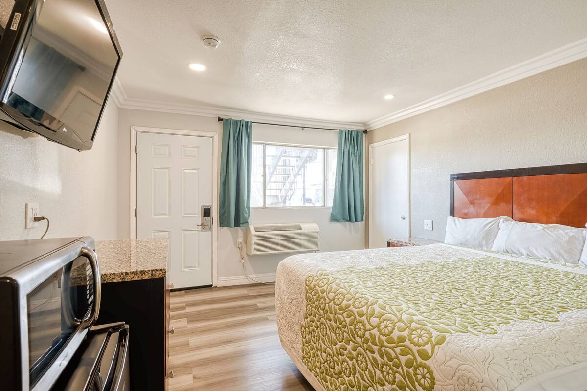 A hotel room with a bed, a television, a microwave, a door, and a window with curtains.