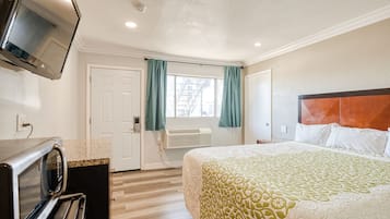 Quarto de hotel com cama, televisão, micro-ondas, porta e janela com cortinas.