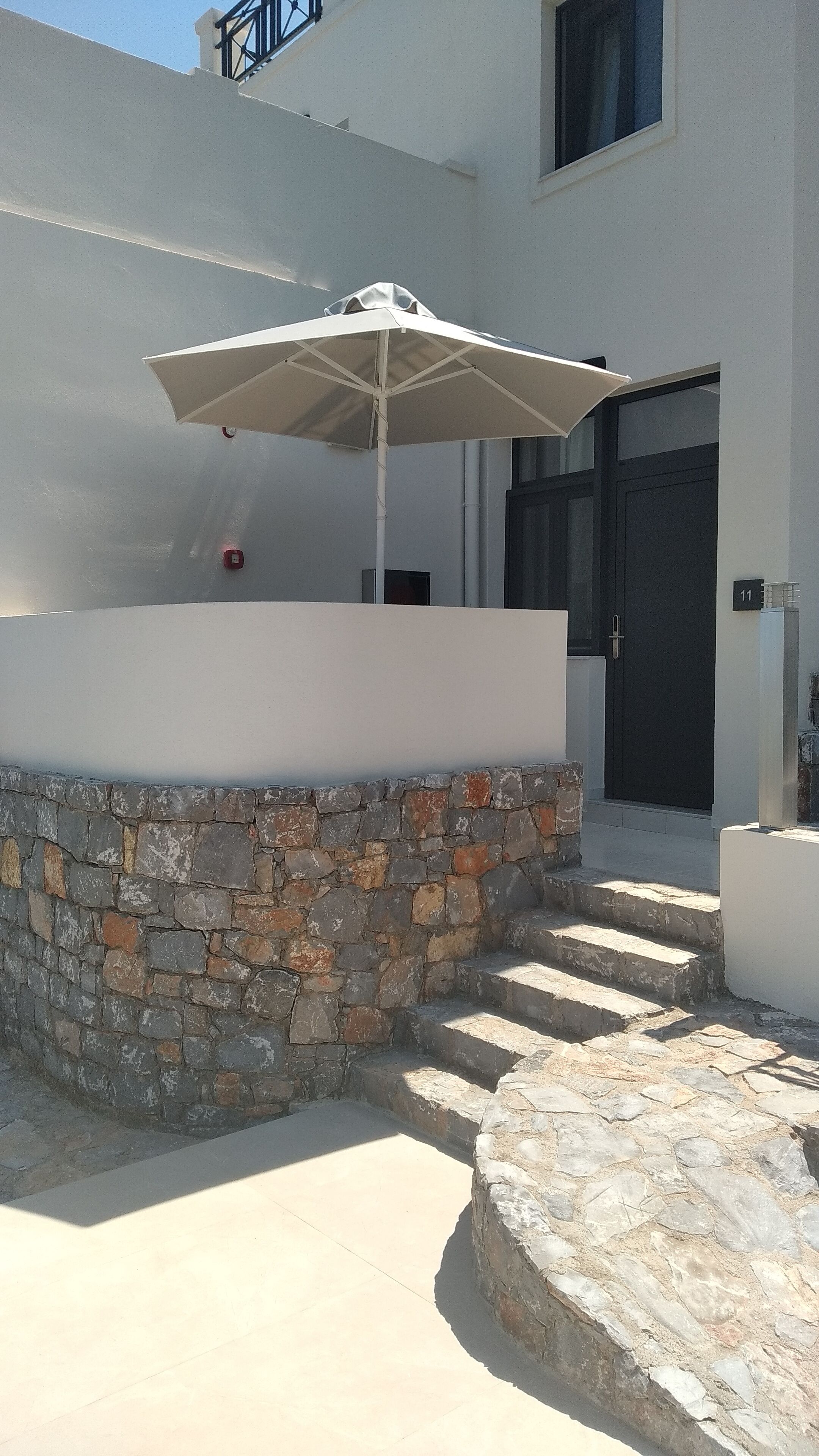 Un muro de piedra con un paraguas blanco, una escalera de piedra y la entrada de un edificio.