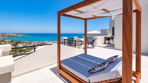 Een balkon met een houten zonnescherm, een enkel bed met kussen, en uitzicht op zee en gebouwen.