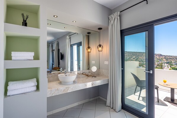 Une salle de bain moderne avec un grand miroir, un lavabo blanc et un balcon vitré agrémenté d’une table et de chaises.