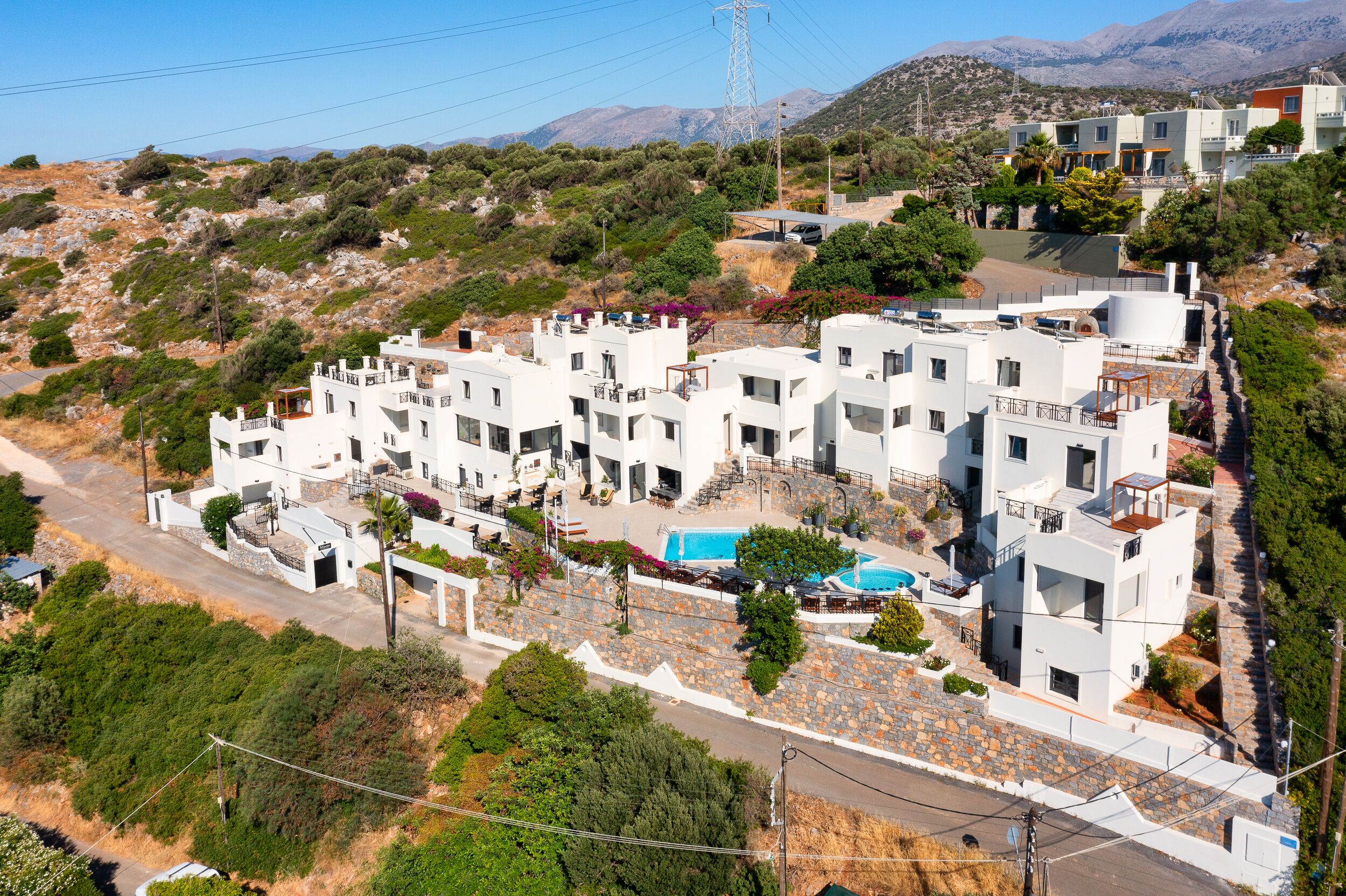 A residential area with modern white buildings, a swimming pool, and a hilly landscape in the background.