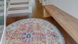 Un pasillo con escalera de madera, un espejo redondo y una alfombra estampada.