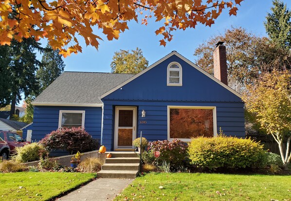 A blue house with a white door, a brick chimney, and a small porch.