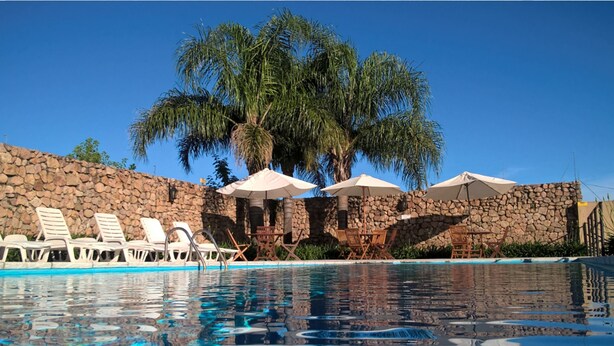 Un área de piscina con sillones de descanso y sombrillas, rodeada de muros de piedra y palmeras.