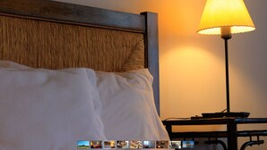 Habitación de hotel con cabecera de madera, cama blanca y una mesa con lámpara.