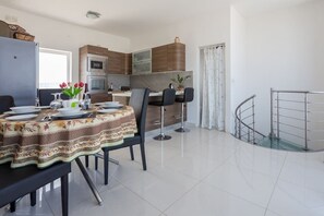 A modern kitchen with wooden cabinets, a dining area with a table set for four, and a staircase with a metal railing.
