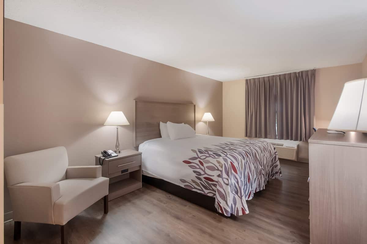 A hotel room with a bed, bedside tables, a chair, and a desk.