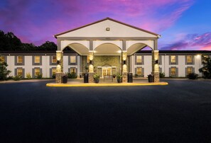 Stately hotel entrance with a central pediment and columns, flanked by double doors and potted plants.