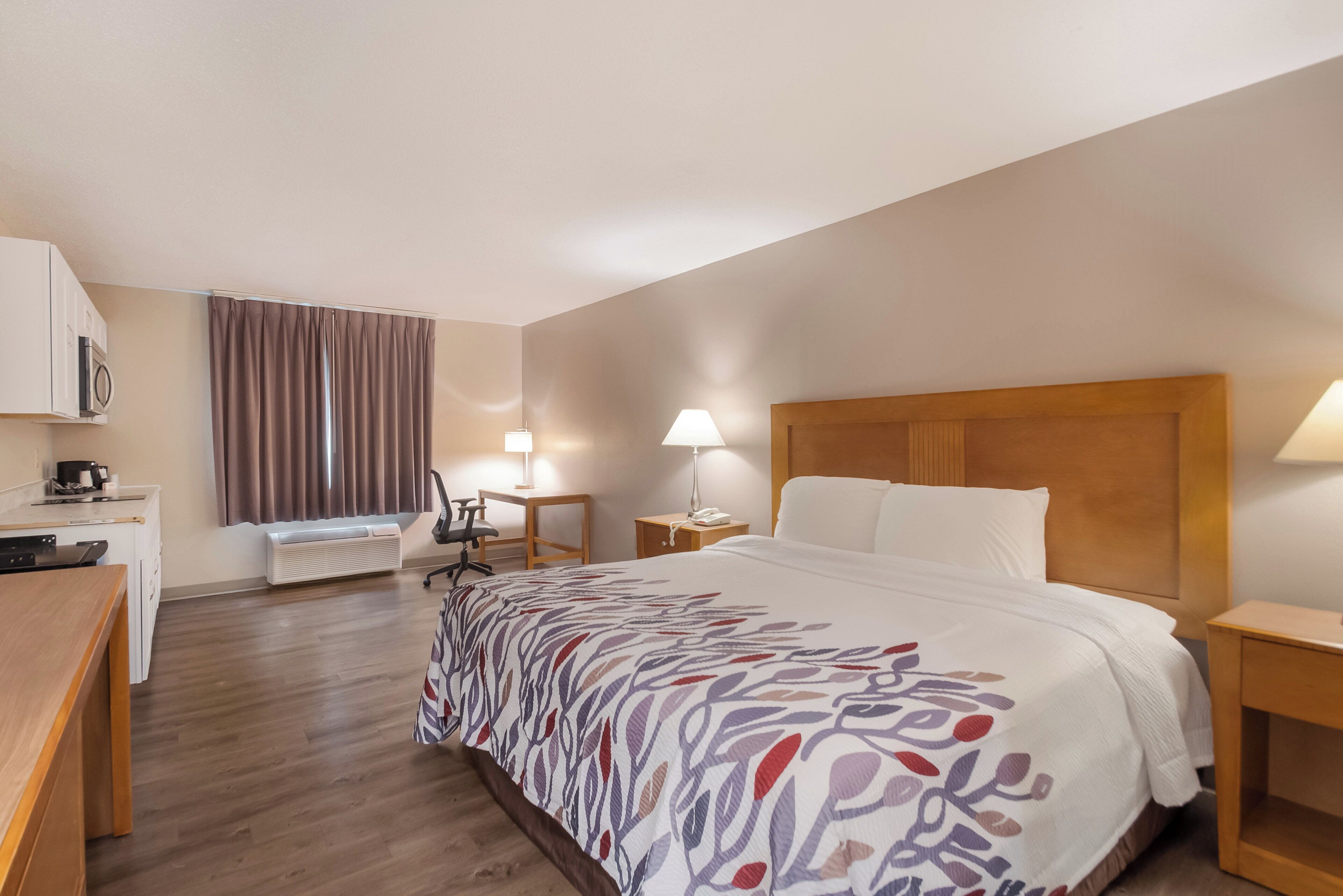 A hotel room with a bed, a desk, a chair, a lamp, and a heater.
