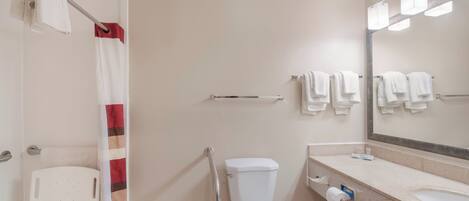 A bathroom with a toilet, a sink, a shower with a curtain, and a mirror with multiple lights.