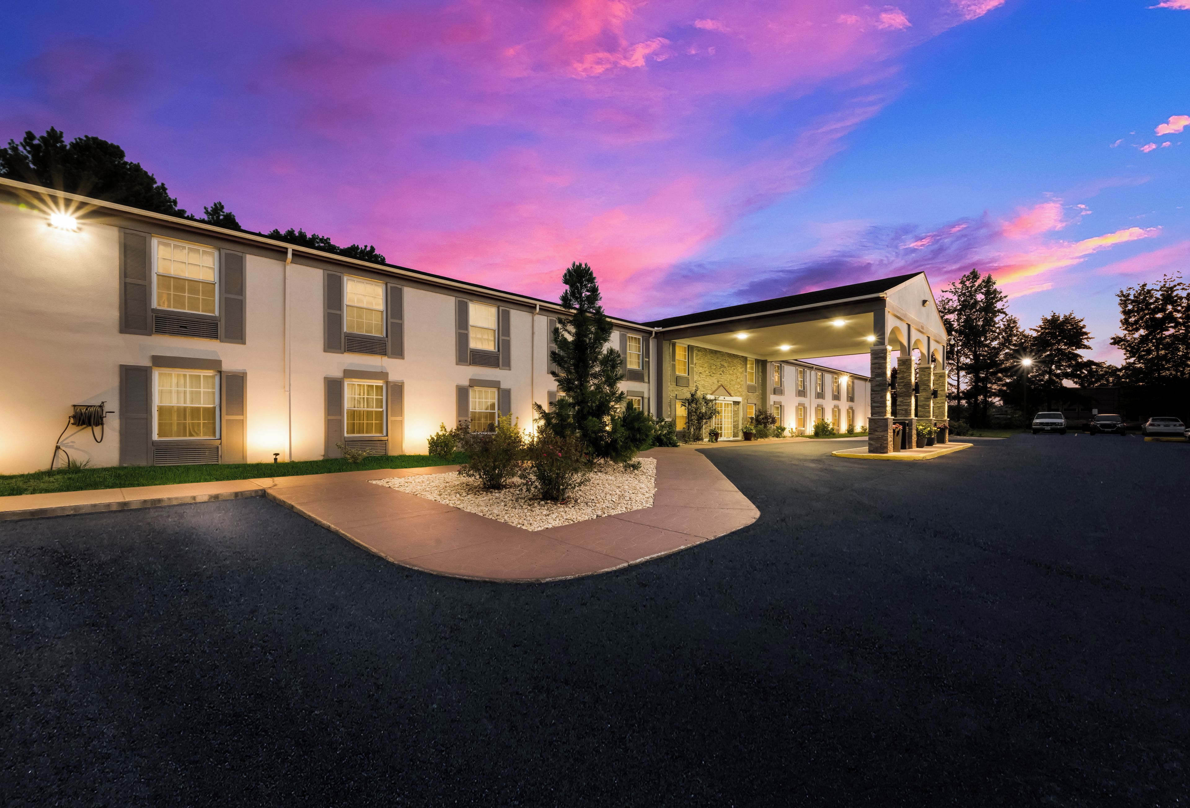 A hotel with a covered outdoor area, a landscaped driveway, and a parking lot.