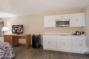 A hotel room with a bed, a desk with a TV, a refrigerator, a microwave, and a kitchenette with cabinets. - Red Roof Inn Dahlgren - Naval Base (King George)