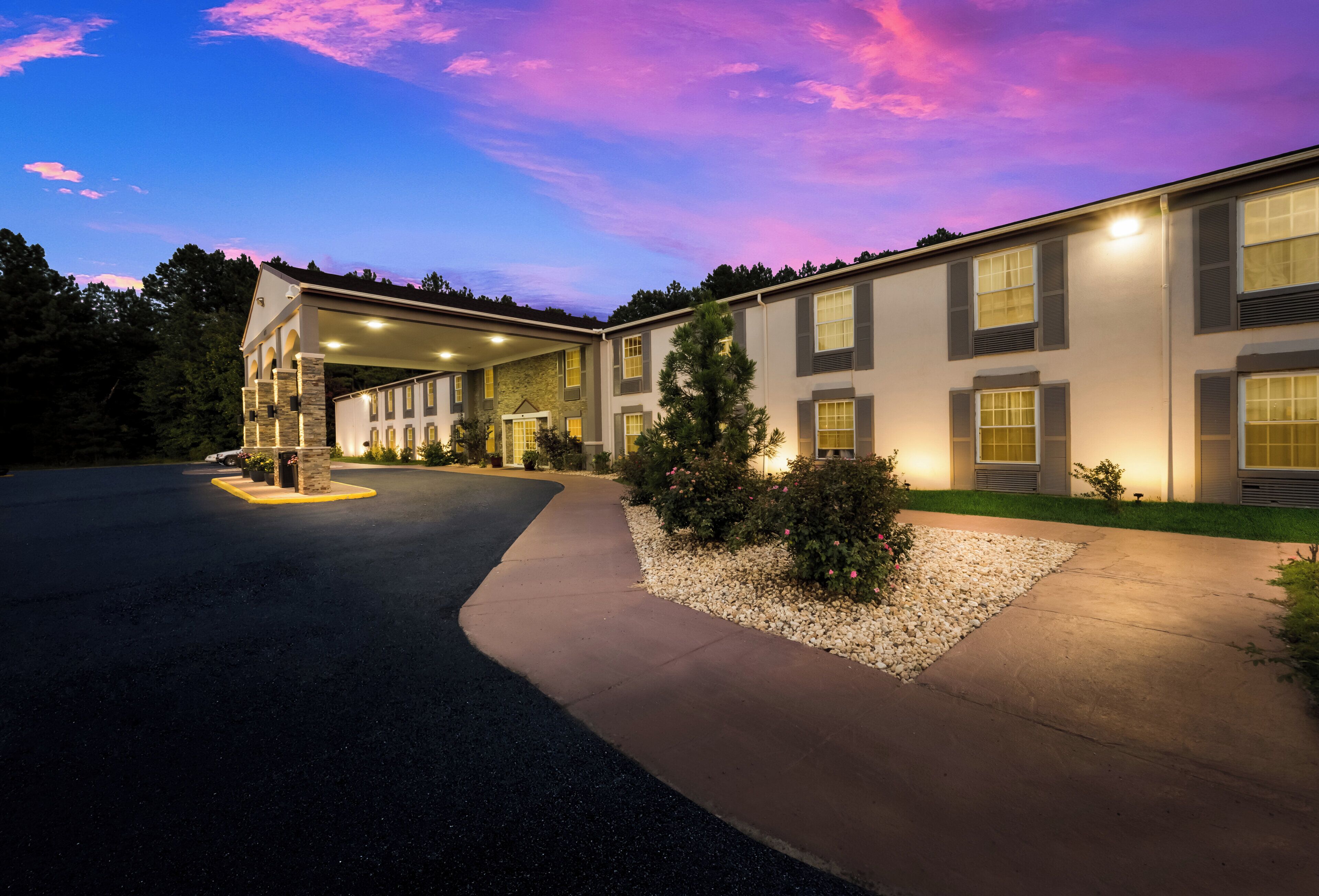 A hotel with a covered parking area, a landscaped garden, and a building with multiple windows and a stone facade.
