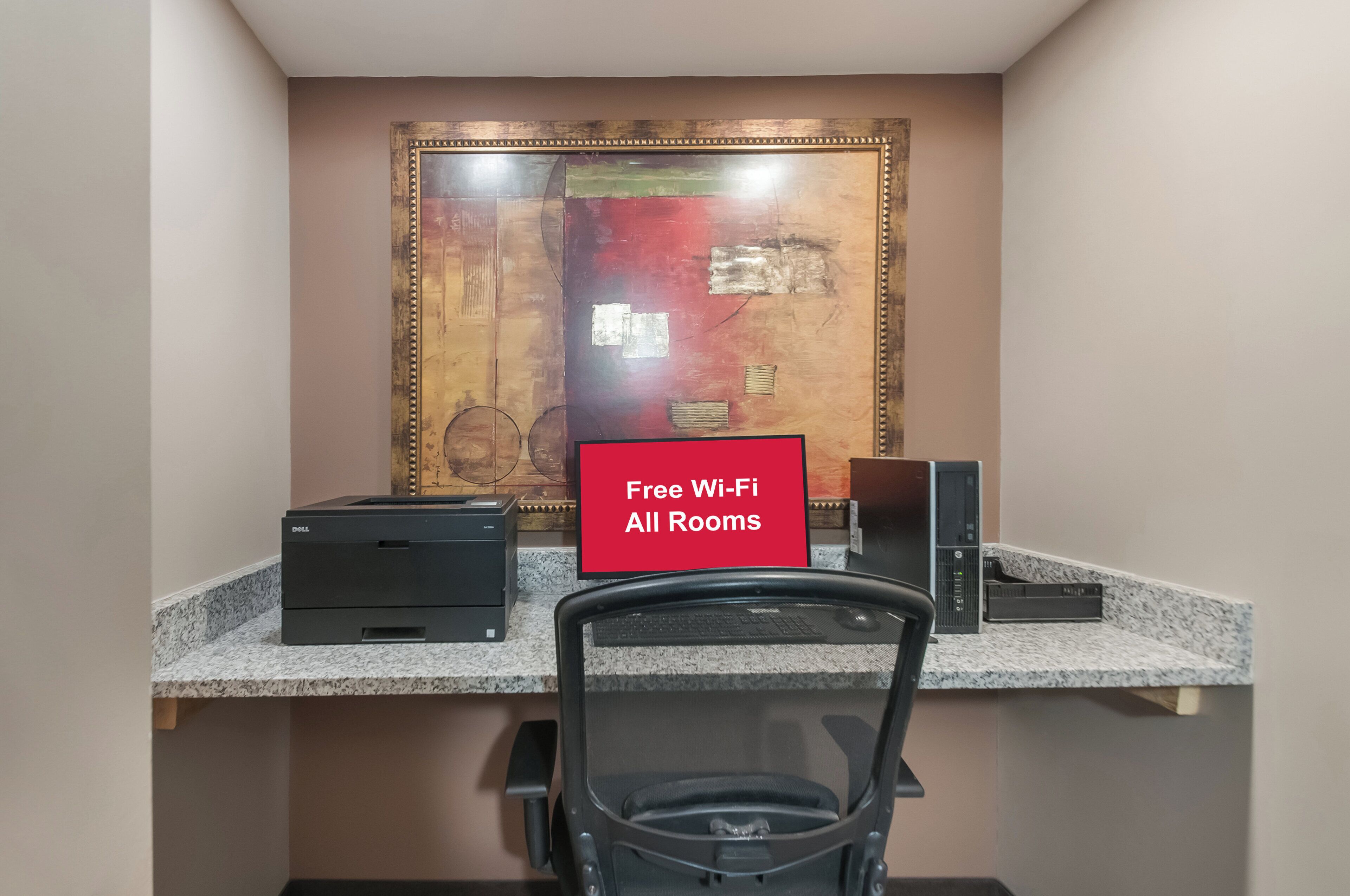 Et arbejdsområde med et skrivebord, to printere, en stol og et skilt på væggen, der angiver gratis Wi-Fi.