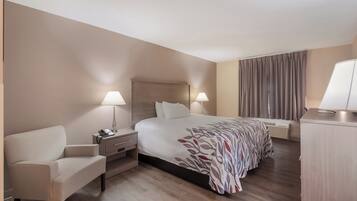 Habitación de hotel con cama, mesitas de noche, una silla, escritorio y ventana con cortinas.