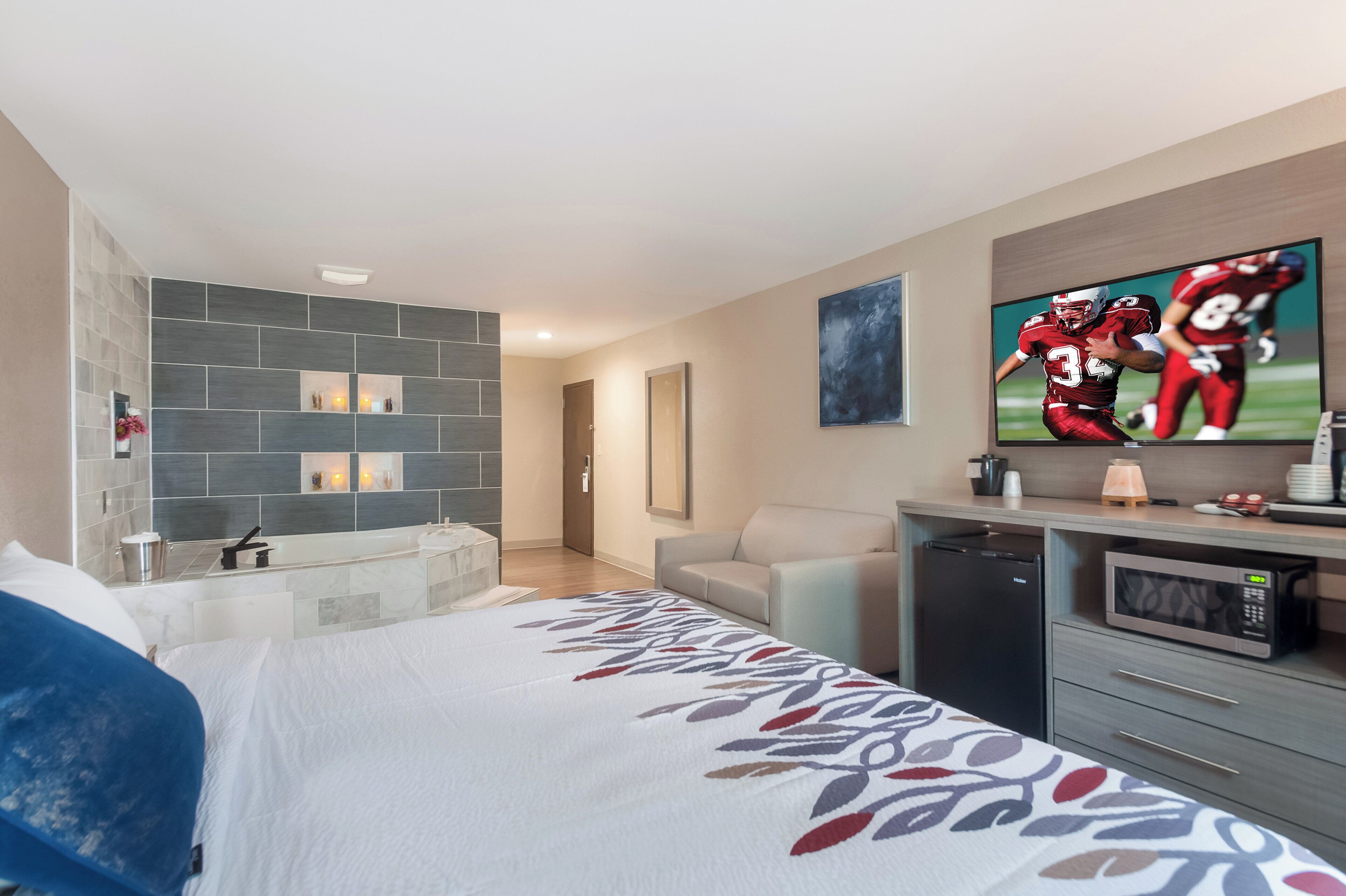 Habitación de hotel con cama, televisión, escritorio con microondas y baño con bañera.