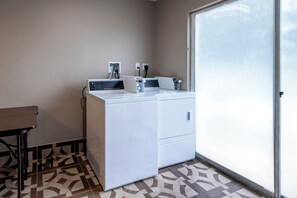 A compact laundry area with a washing machine, a dryer, and a small table. - Red Roof Inn Dahlgren - Naval Base (King George)