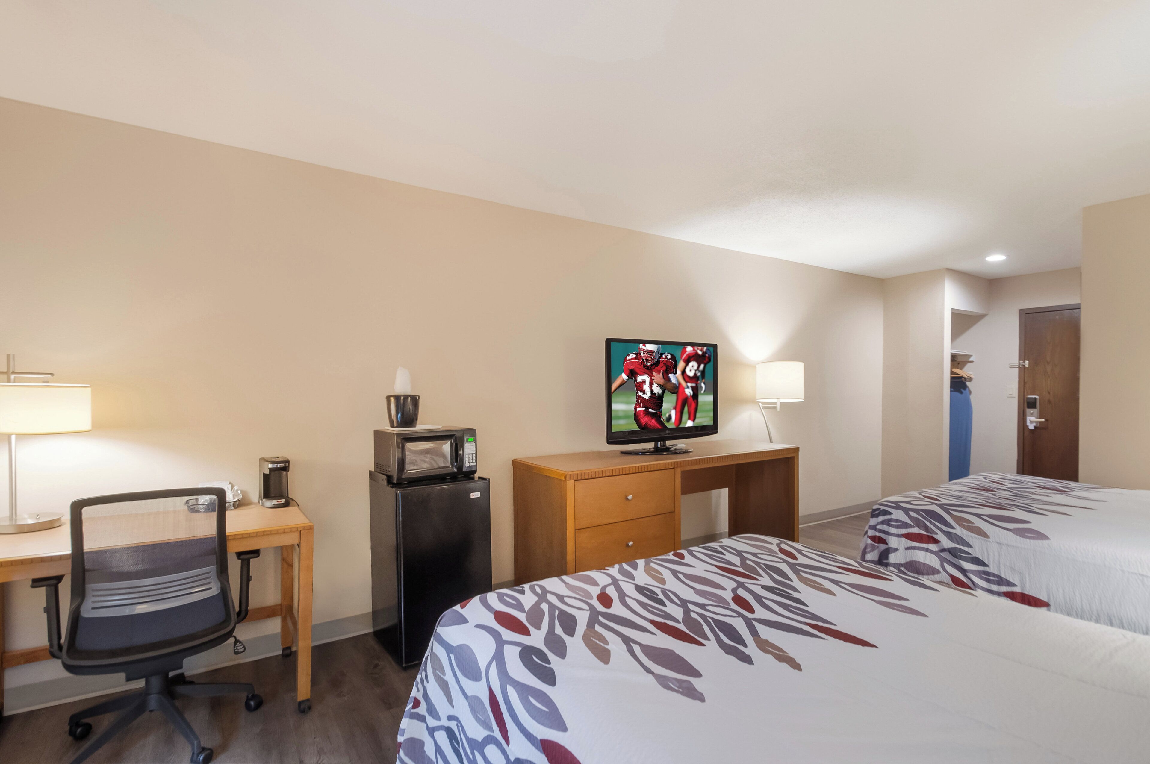 A hotel room with a desk, a refrigerator, a television, a bed, and a door.