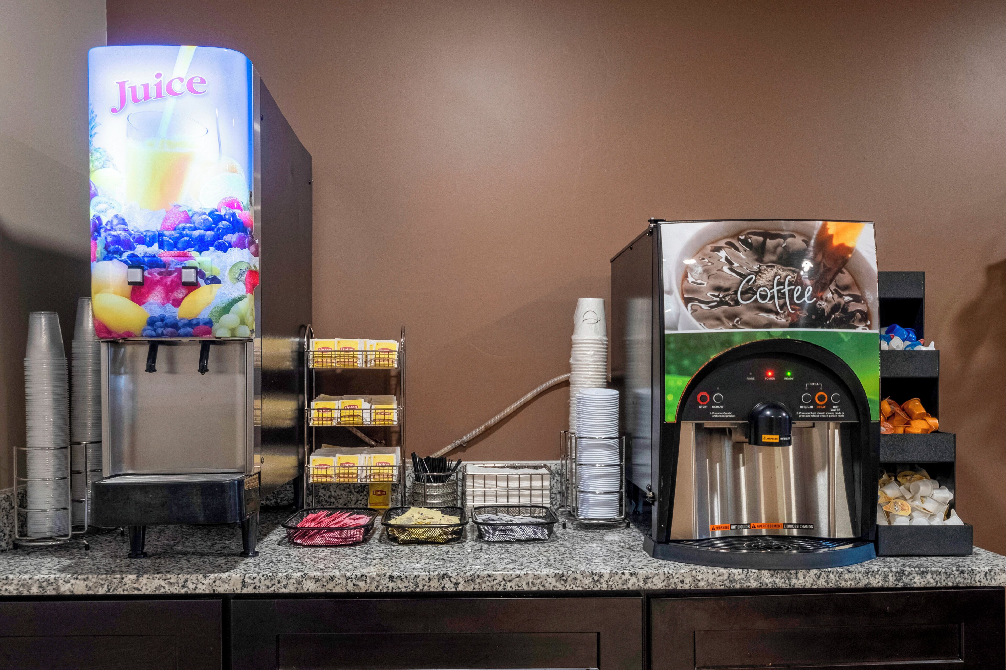 En drikkestasjon med en juiceuddispenser og en kaffemaskine, begge med tydelige instruktioner og sikkerhedsadvarsler.
