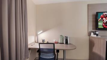 A hotel room with a desk, chair, television, and a coffee machine.
