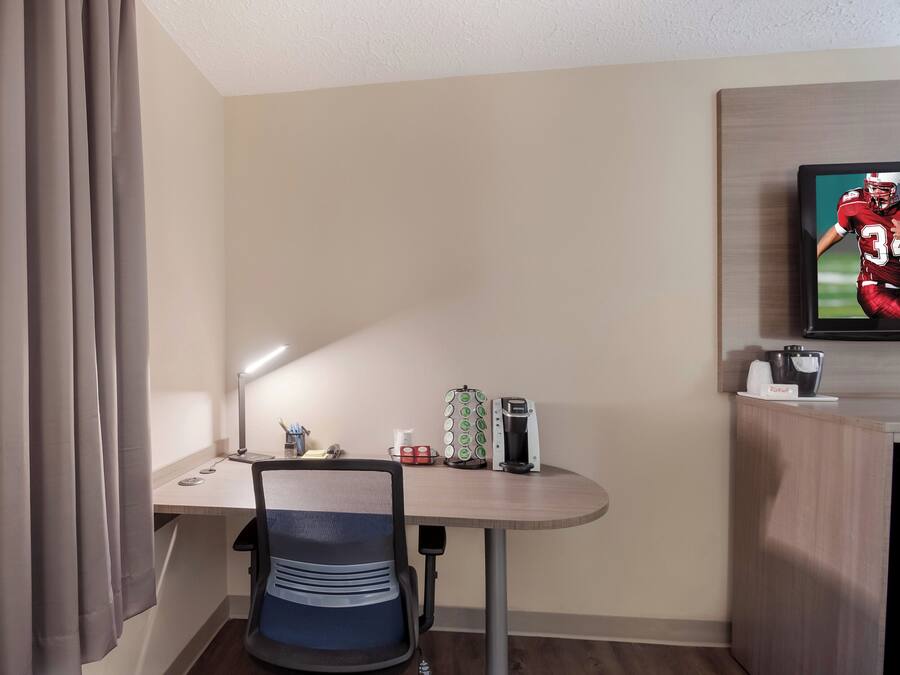 A hotel room with a desk, chair, television, and a coffee machine.