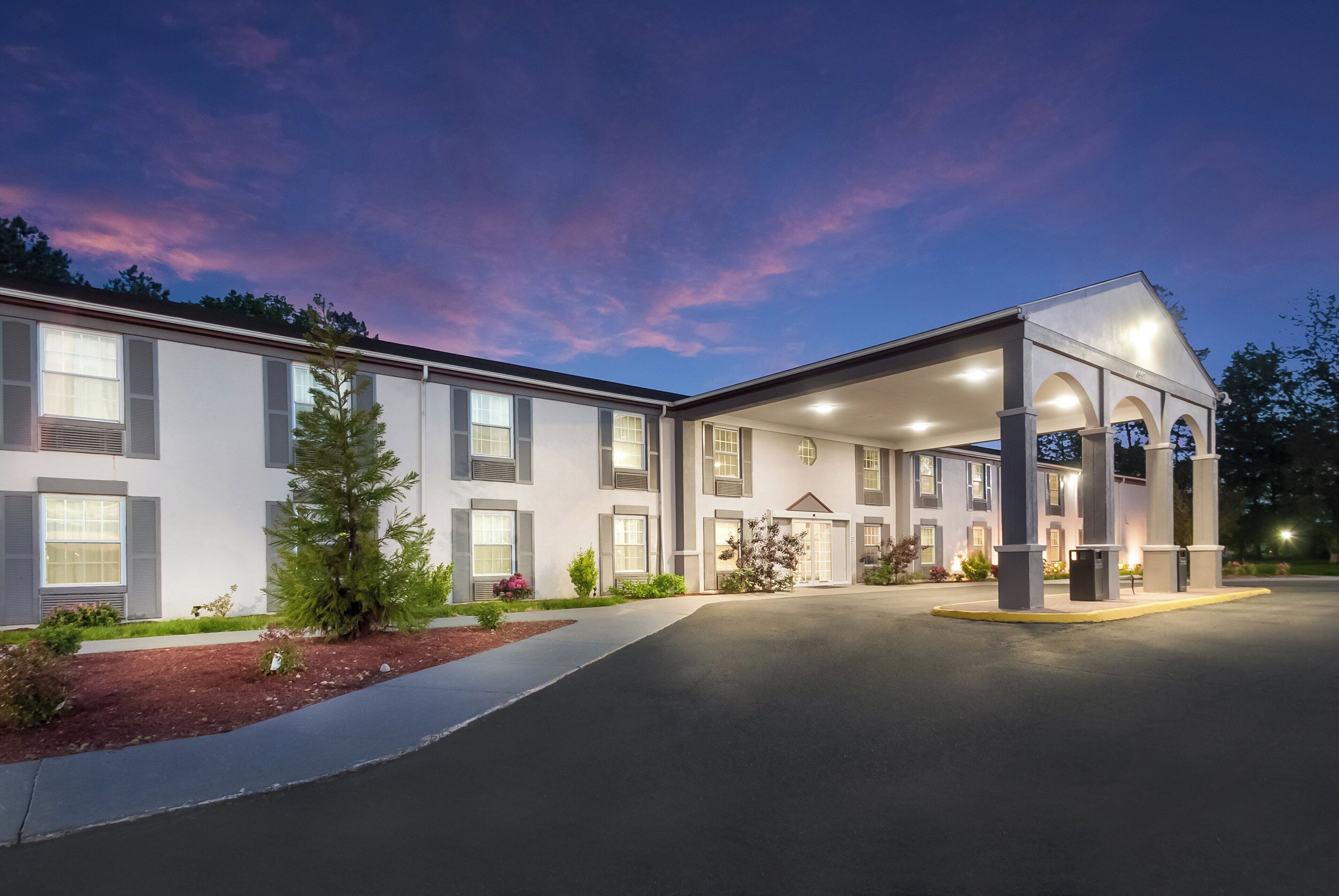 A hotel with a covered entrance, multiple windows, and a landscaped front yard.