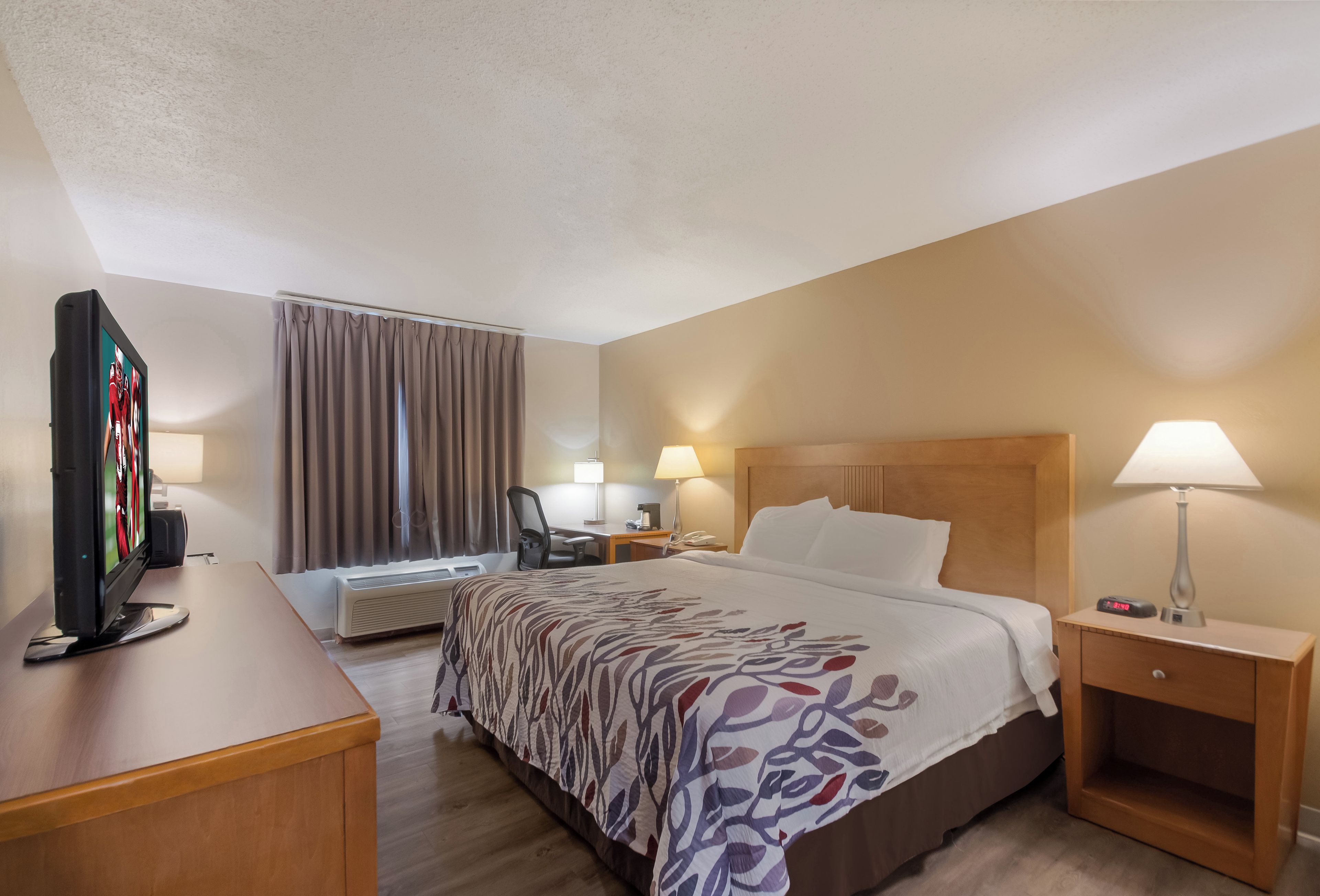 A hotel room with a bed, a desk, a television, a lamp, and a nightstand.