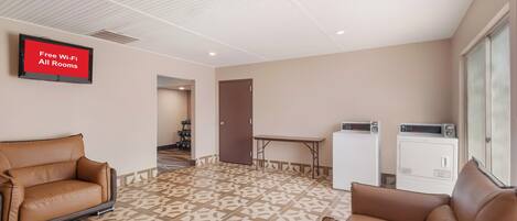 A hotel room with a sofa, a table, a washing machine, and a television displaying 'Free Wi-Fi All Rooms'.