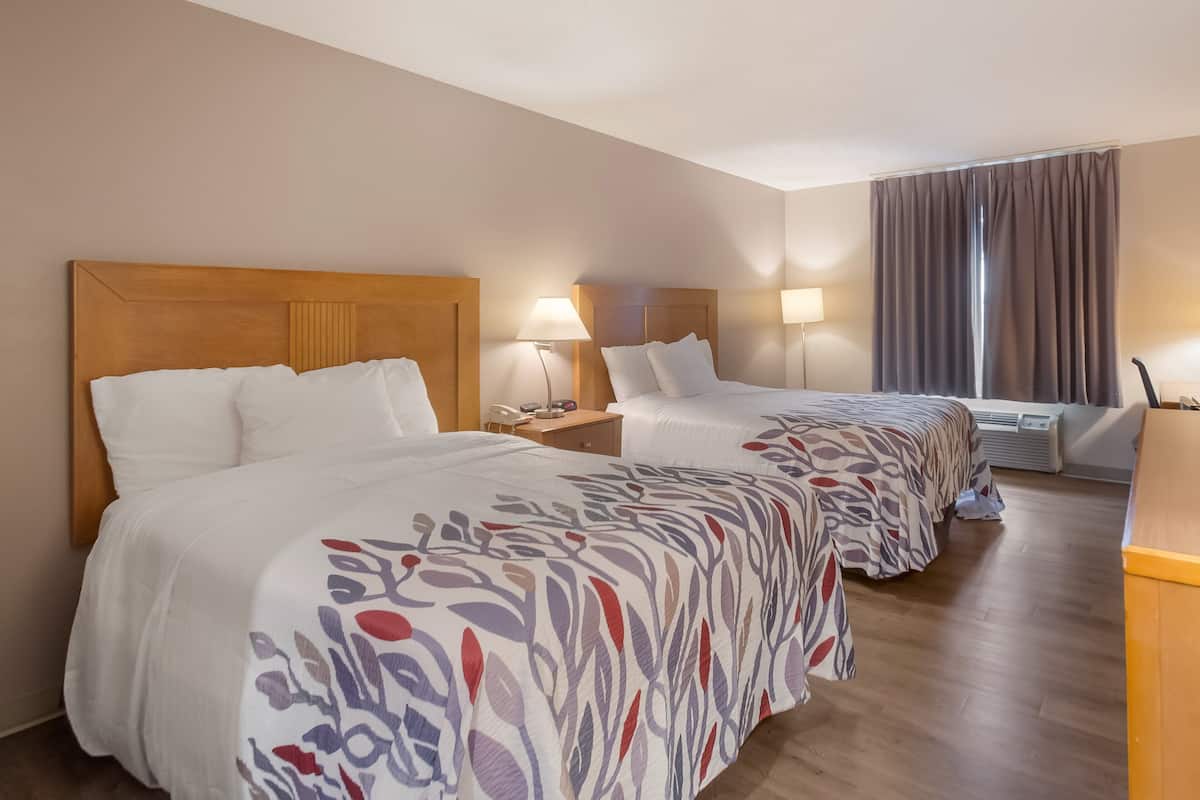 A hotel room with two beds, a desk, a lamp, and a window with curtains.