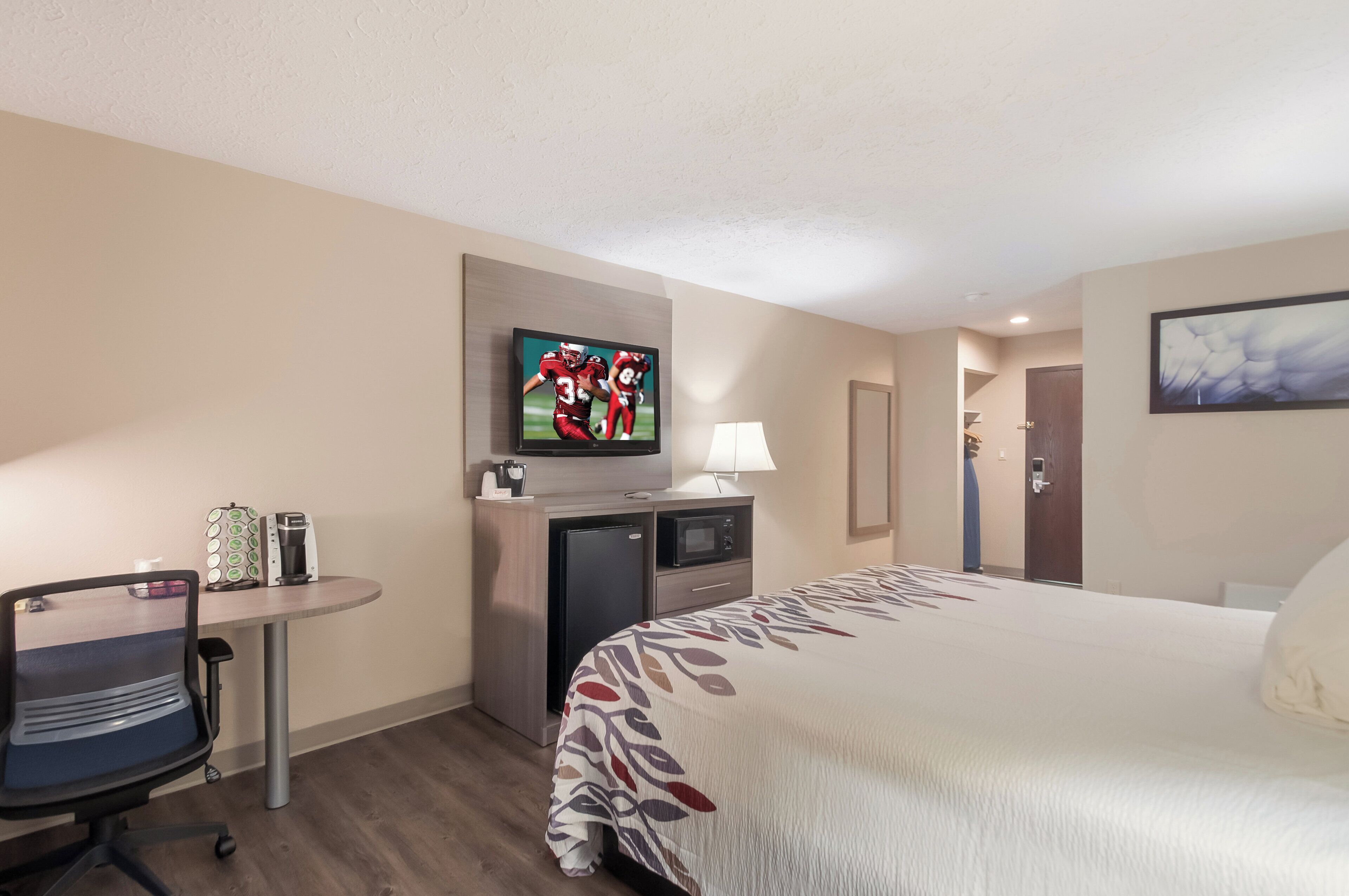 A hotel room with a bed, a desk with a chair, a television, a coffee maker, and a microwave.