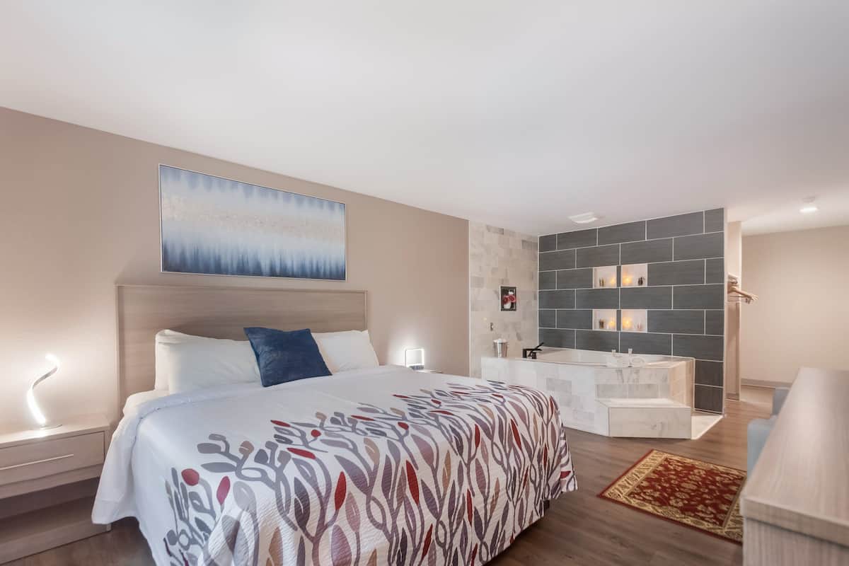 A modern hotel room with a large bed, a bedside table with a lamp, a bathroom with a marble sink, and a decorative wall.