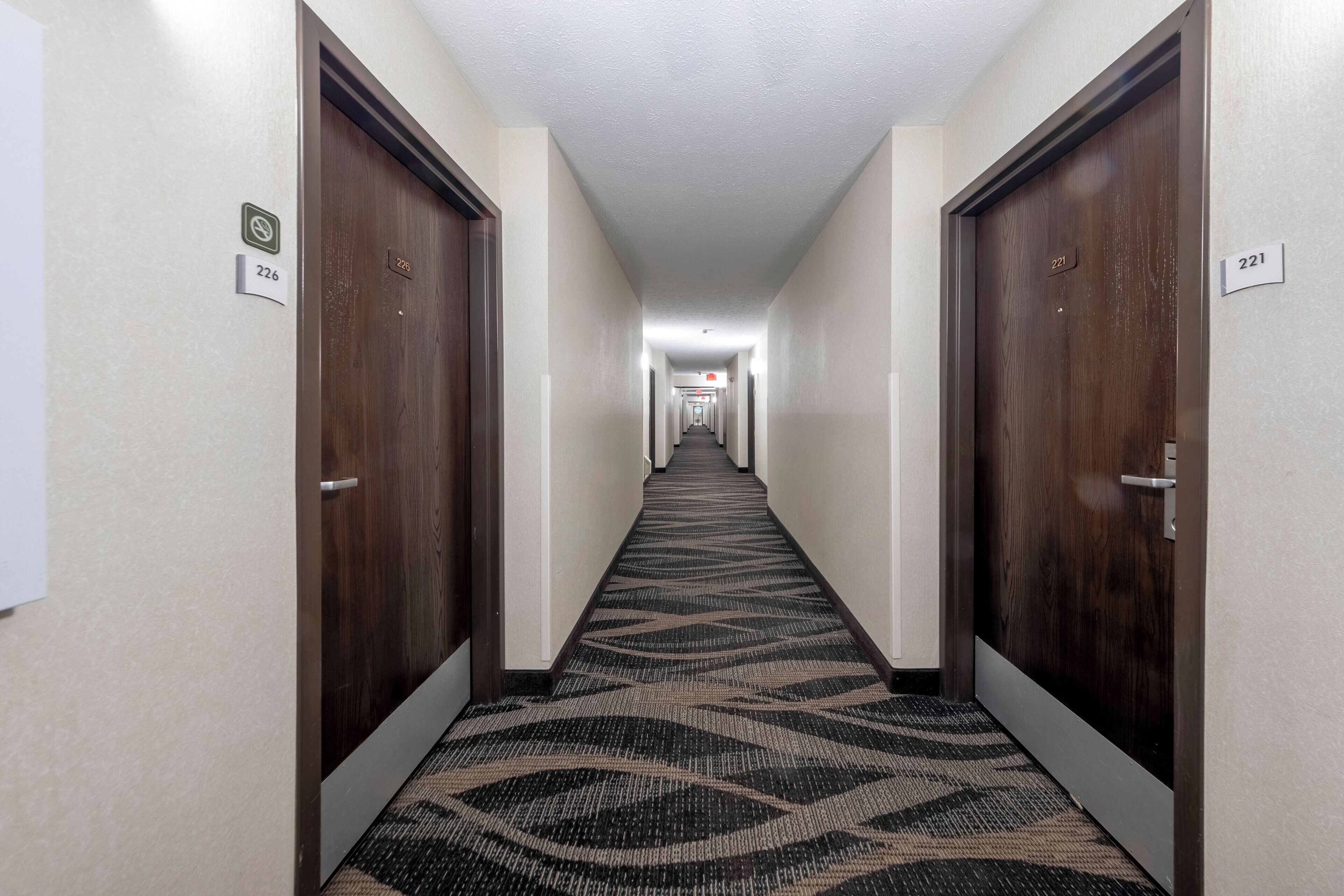 A hotel hallway with carpeted floors, wooden doors, and numbered room signs.