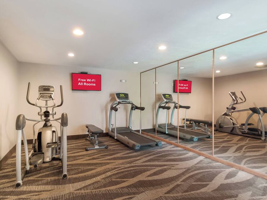 A fitness room with exercise equipment, a mirror, and a sign indicating free Wi-Fi availability.