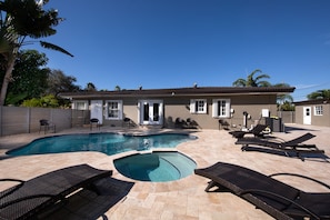 A swimming pool with lounge chairs and a house in the background.