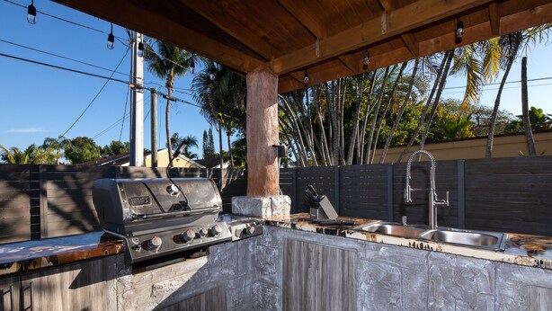 Une cuisine extérieure équipée d’un barbecue, d’un évier et d’un plan de travail en bois.