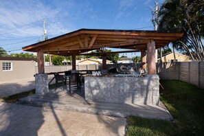 A barbecue area with a wooden pergola, stone counter, and outdoor seating.