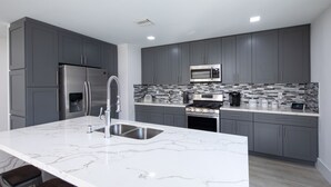 Une cuisine moderne avec des meubles gris, un réfrigérateur en acier inoxydable, un four à micro-ondes et une cuisinière à gaz.