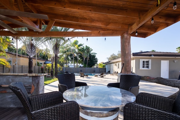 An outdoor patio with wicker furniture, a pool, and a covered area with wooden beams.