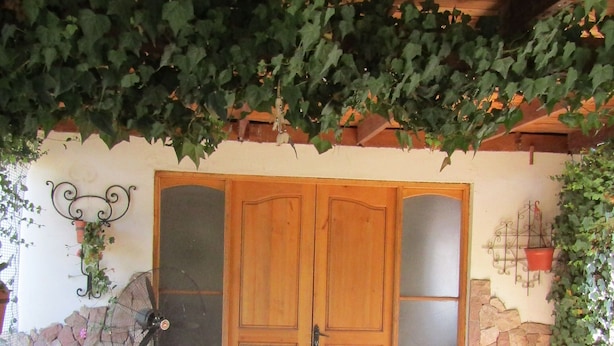 Eine Außenpatio mit Holztisch und -stühlen, einer Steinmauer und einer Holztür.