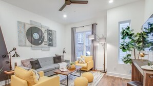 Ein modernes Wohnzimmer mit einem grauen Sofa, gelben Ohrensesseln, einem Couchtisch und einem großen Fenster mit Pflanzen.