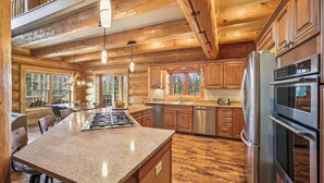 A spacious kitchen with wooden cabinets, a granite countertop, stainless steel appliances, and a large island. - Fireside Retreat: Highlands Log Home, Hot Tub & Fireplace, Peak Views! (Breckenridge)