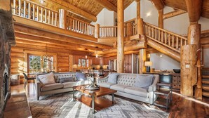 A spacious log cabin interior with a large living area, a fireplace, and a wooden staircase. - Fireside Retreat: Highlands Log Home, Hot Tub & Fireplace, Peak Views! (Breckenridge)
