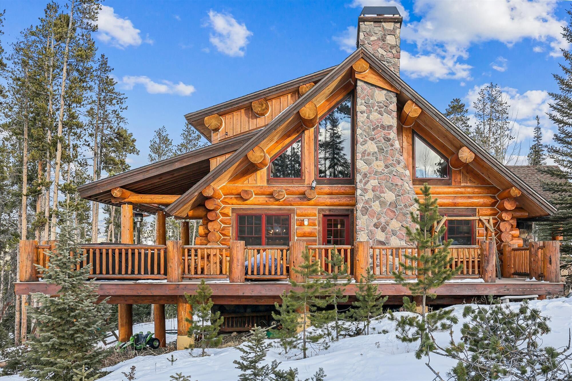 A log cabin with a stone chimney, wooden balconies, and a snow-covered landscape.