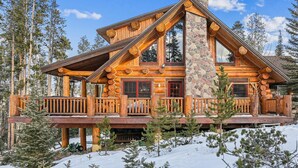 A log cabin with a stone chimney, wooden balconies, and a snow-covered landscape. - Fireside Retreat: Highlands Log Home, Hot Tub & Fireplace, Peak Views! (Breckenridge)