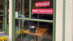 Ventana de restaurante con un letrero que dice 'Riverfront Wood Fired Pizza'.