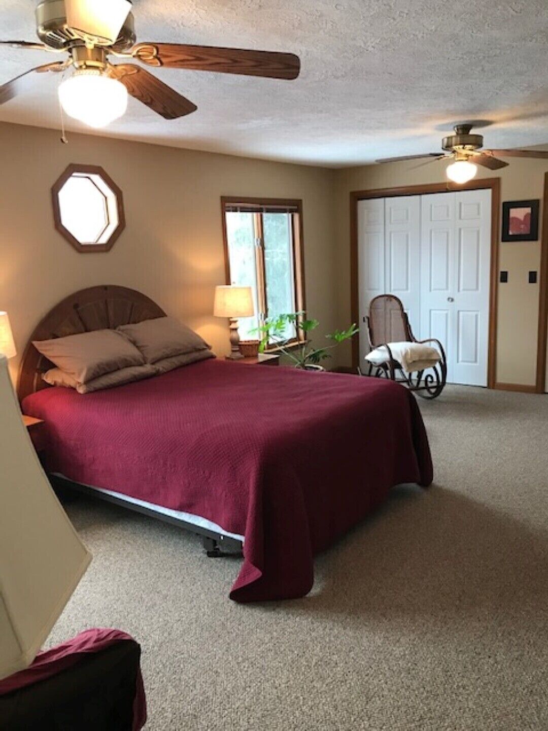 A bedroom with a bed, two wall-mounted lamps, a ceiling fan, a window, and a door.
