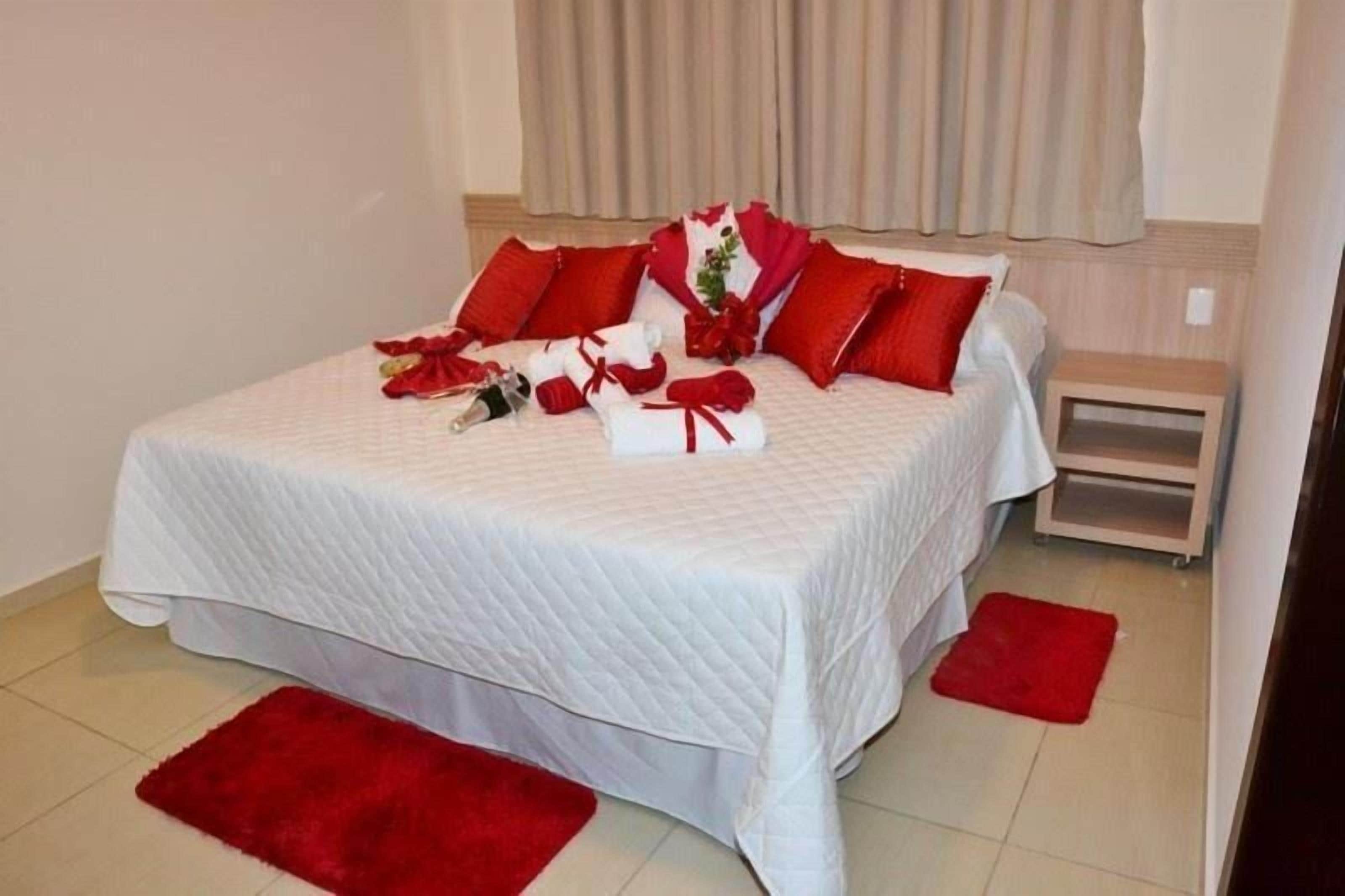 A neatly made bed with red pillows and a bouquet of flowers.