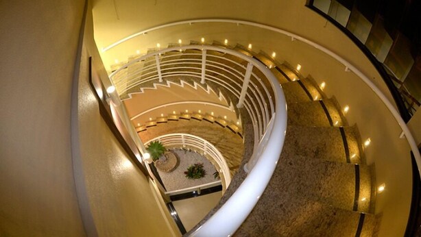 Una escalera de caracol con un jardín central, rodeada por una barandilla blanca e iluminada por luces colgantes.